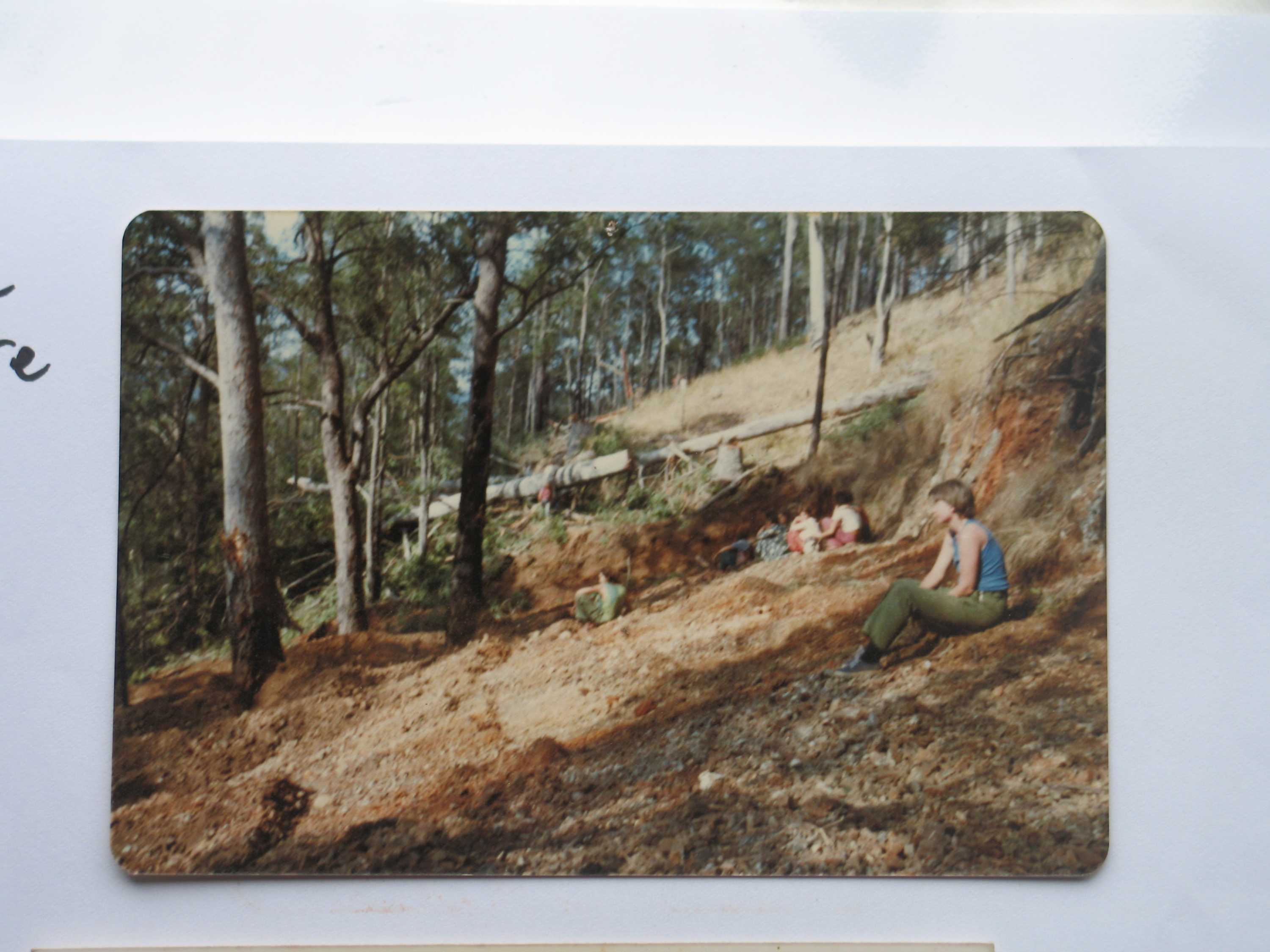 Wide colour archive shot of numerous women scattered across the top of a clearing bulldozed in the bush.
