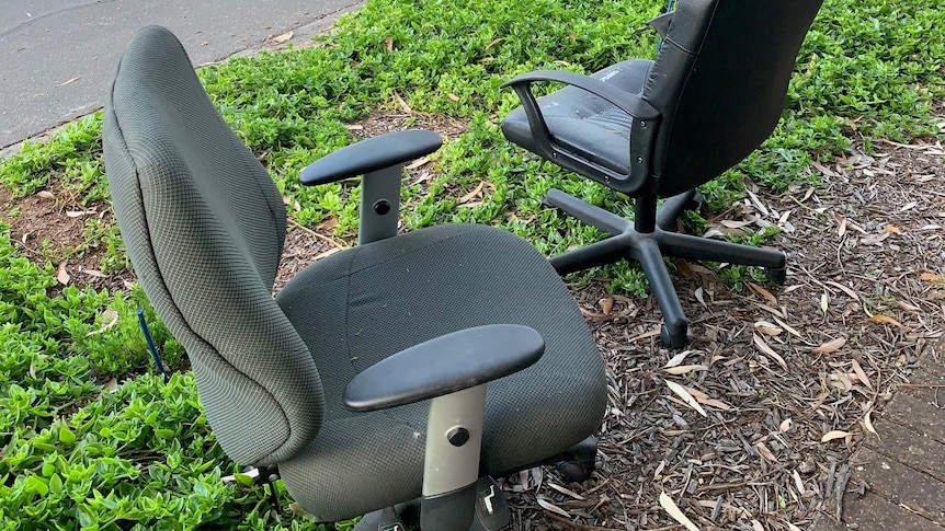 two black office chairs on a green verge with a street in the background