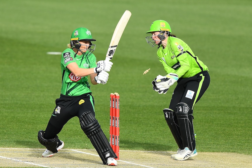Meg Lanning attempts to hit the ball as it hits the stumps and the bails fly off.