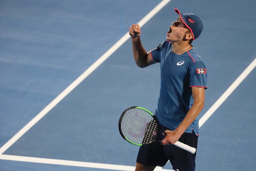 Alex de Minaur looks to the left with a shocked expression on his face and mouth open as he raises a fist on tennis court.