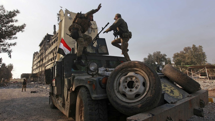Members of the Iraqi rapid response forces stand on the top of a vehicle.