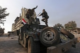 Members of the Iraqi rapid response forces stand on the top of a vehicle.