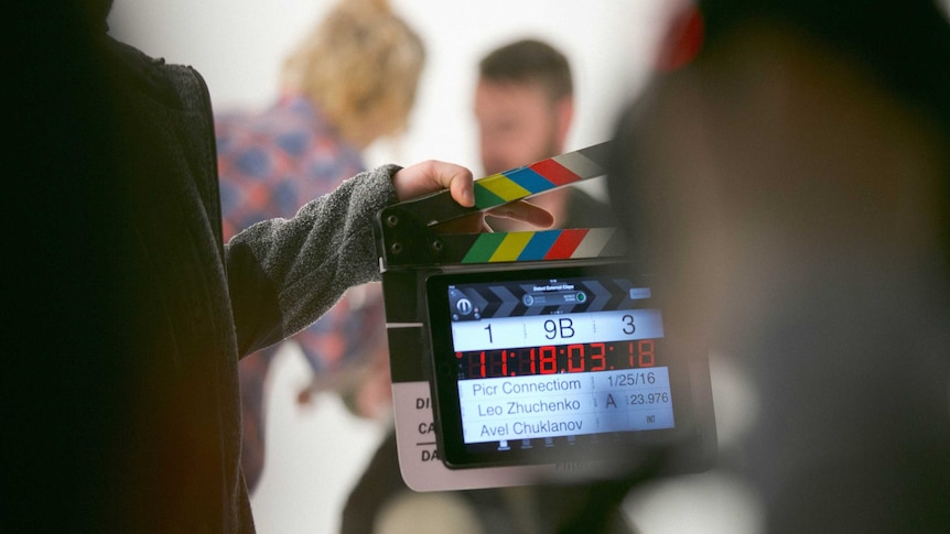 A person holds a clapperboard in front of a scene on a movie set