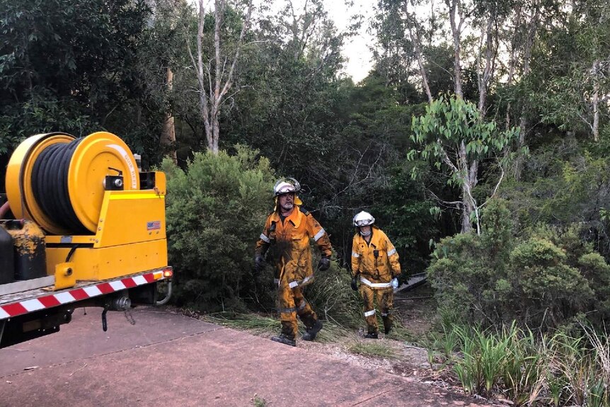 Two fire fighters walk out of the bush blackened by soot.