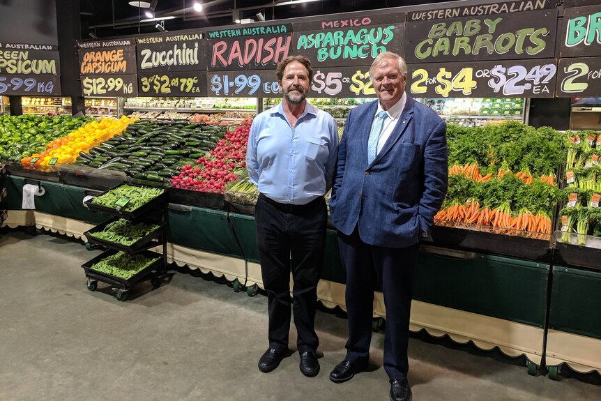 Two men standing in front of a fruit and vegetable aisle in farmers market