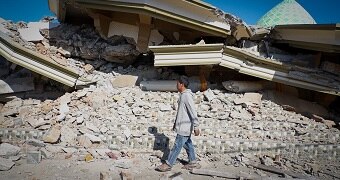 Lalu Fauzan walks beside the towering pile of rubble that used to be his village mosque.