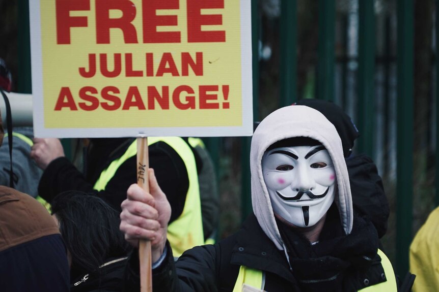 A mask-wearing supporter of Julian Assange holds a sign saying 'Free Julian Assange!'