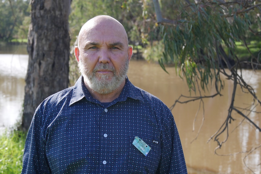 A bald man standing in front of a river 