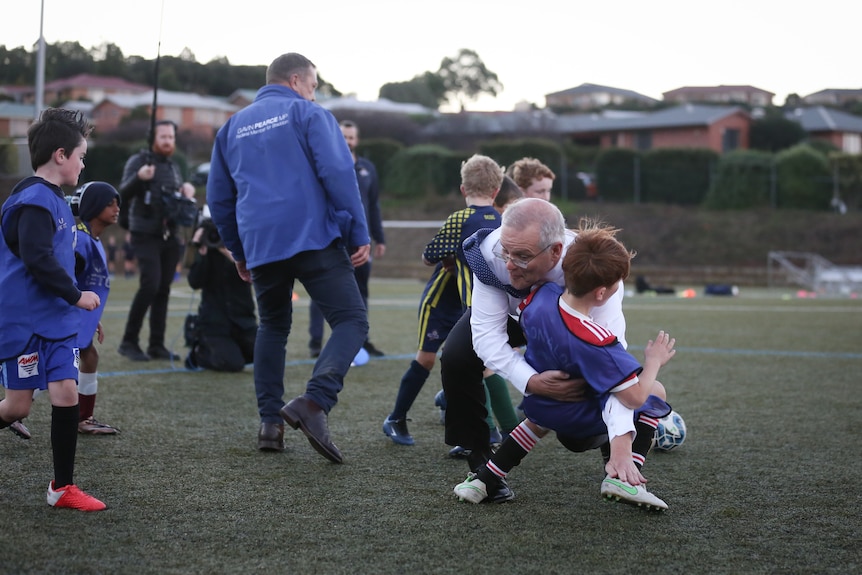A man in a suit barges into a child on a soccer field