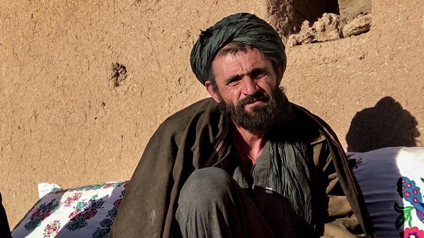 Sayed Hamid Khan, with a beard and black hair, wearing a green turban, sits outside in front of a pale brown wall.