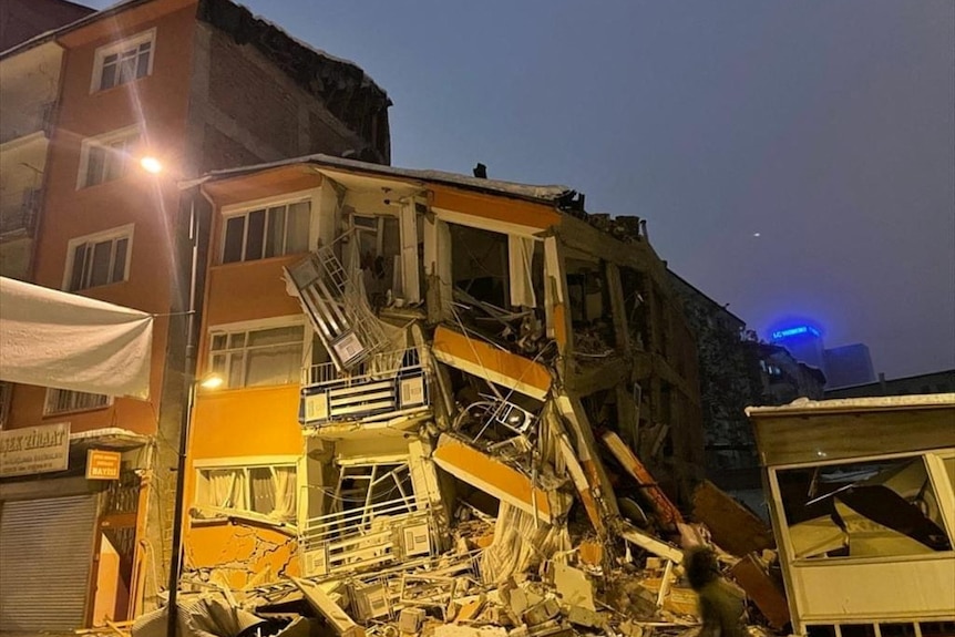 A collapsed building can be seen at night following an earthquake in Türkiye