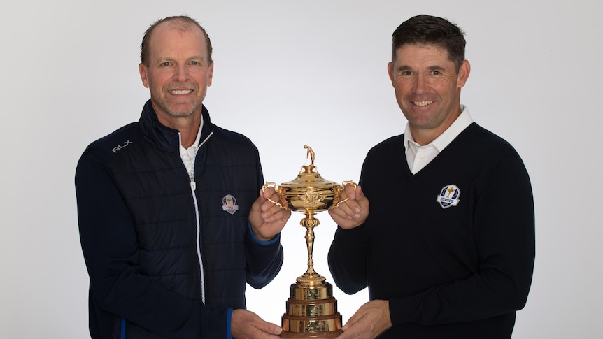 Two retired male golfers stand holding the Ryder Cup trophy.