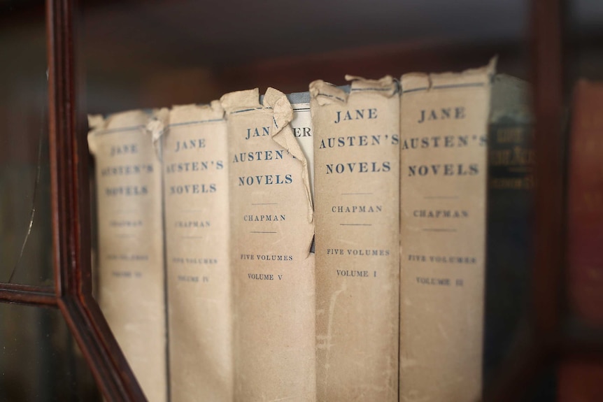 A line of Jane Austen's complete works, aged and worn books.