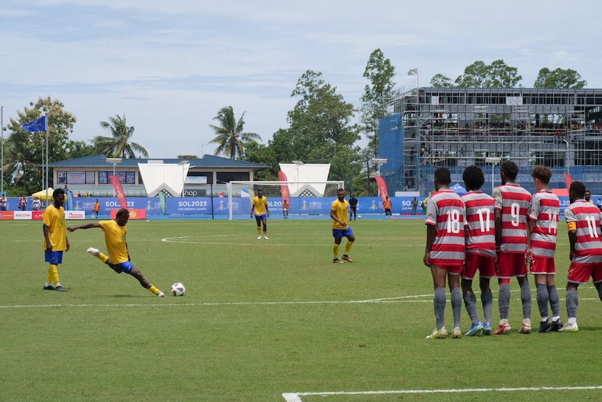 A Solomon Islands player prepares to kick the ball. A line of New Caledonian players stand in the way.
