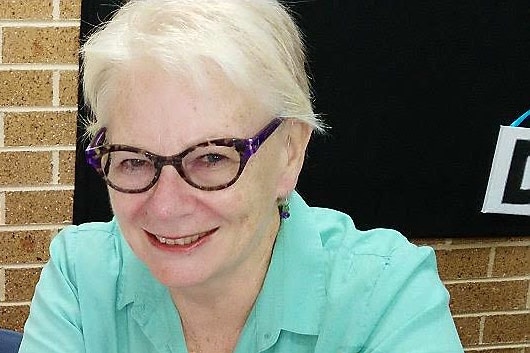 Headshot of an older woman sitting in front of a vase of flowers.