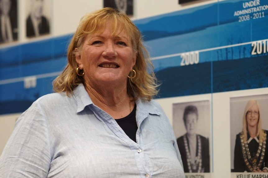 A woman stands in front of a wall featuring many portrait photos.