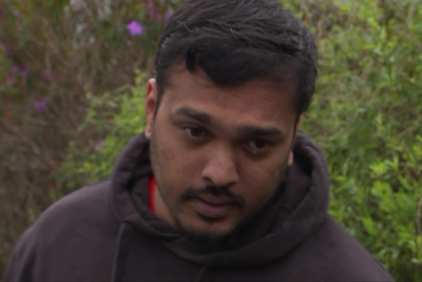 a man in a black hoody speaking into the camera