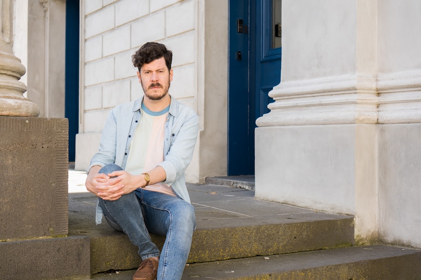 A dark-haired man sits on steps outside a building.