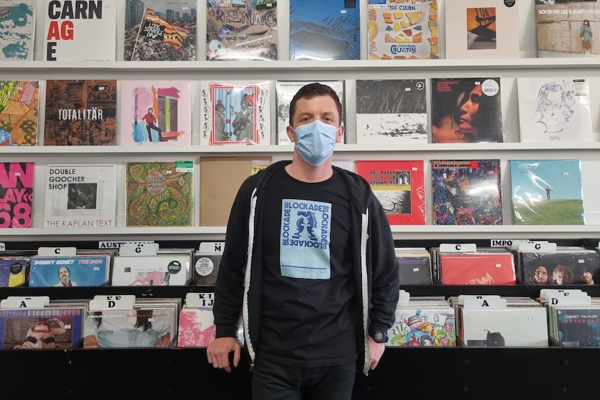 A masked man stands in front of a wall of records