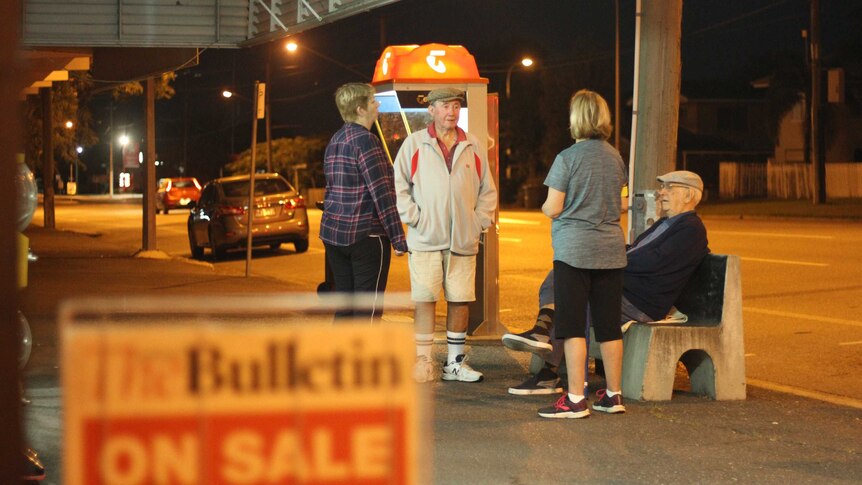 Four people gather outside a newsagent before dawn