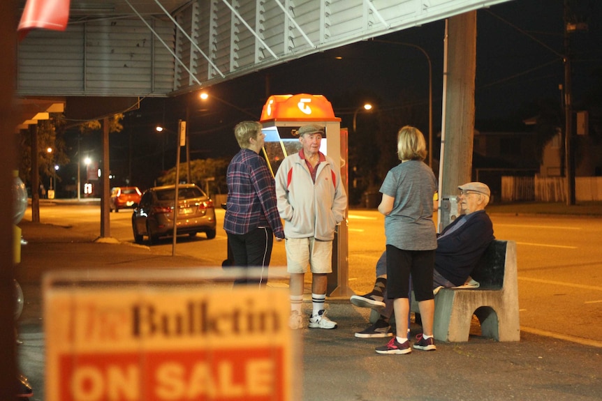 Four people gather outside a newsagent before dawn