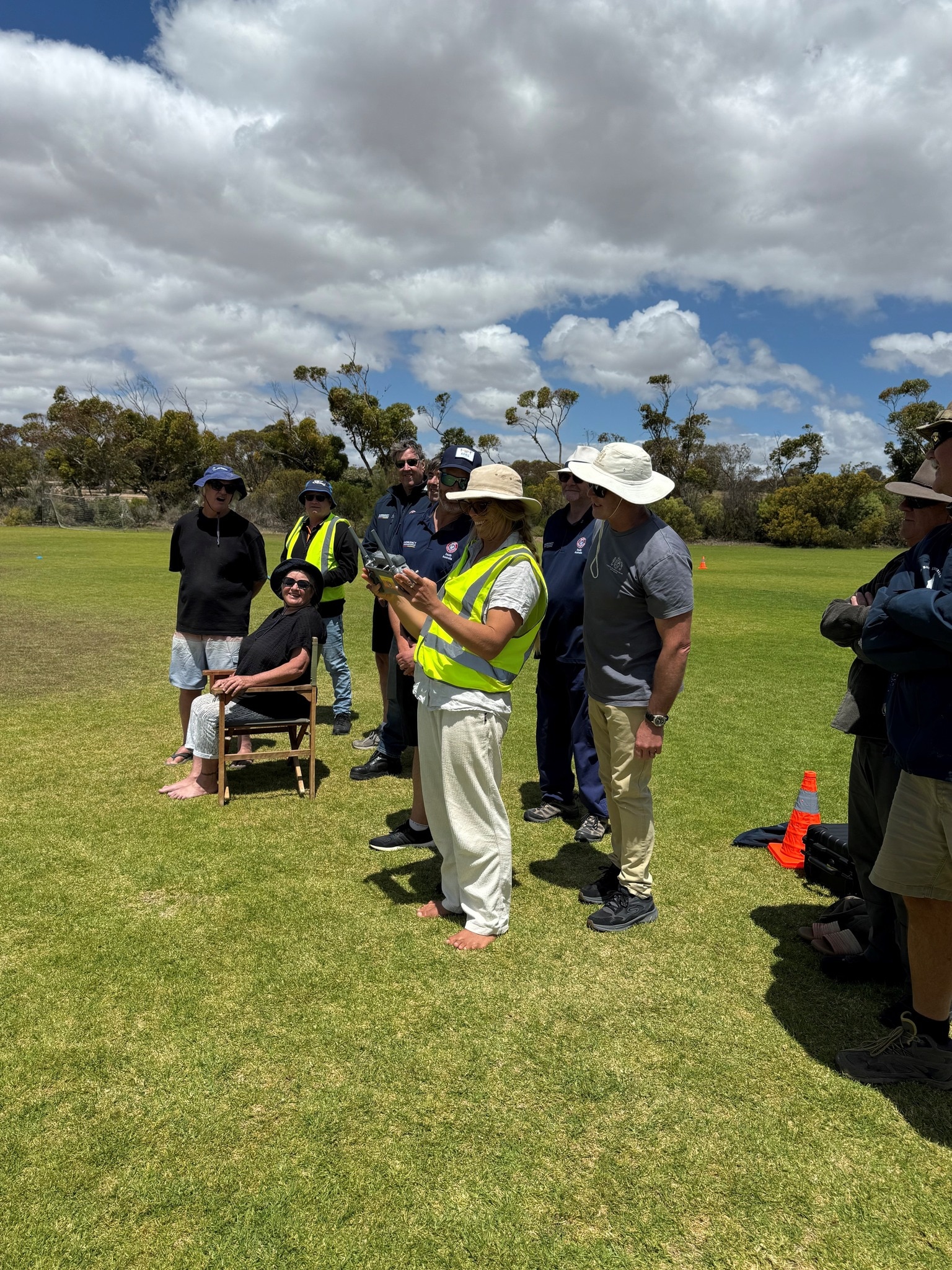 Una mujer con un chaleco reflectante sostiene el control remoto de un dron mientras la gente observa.