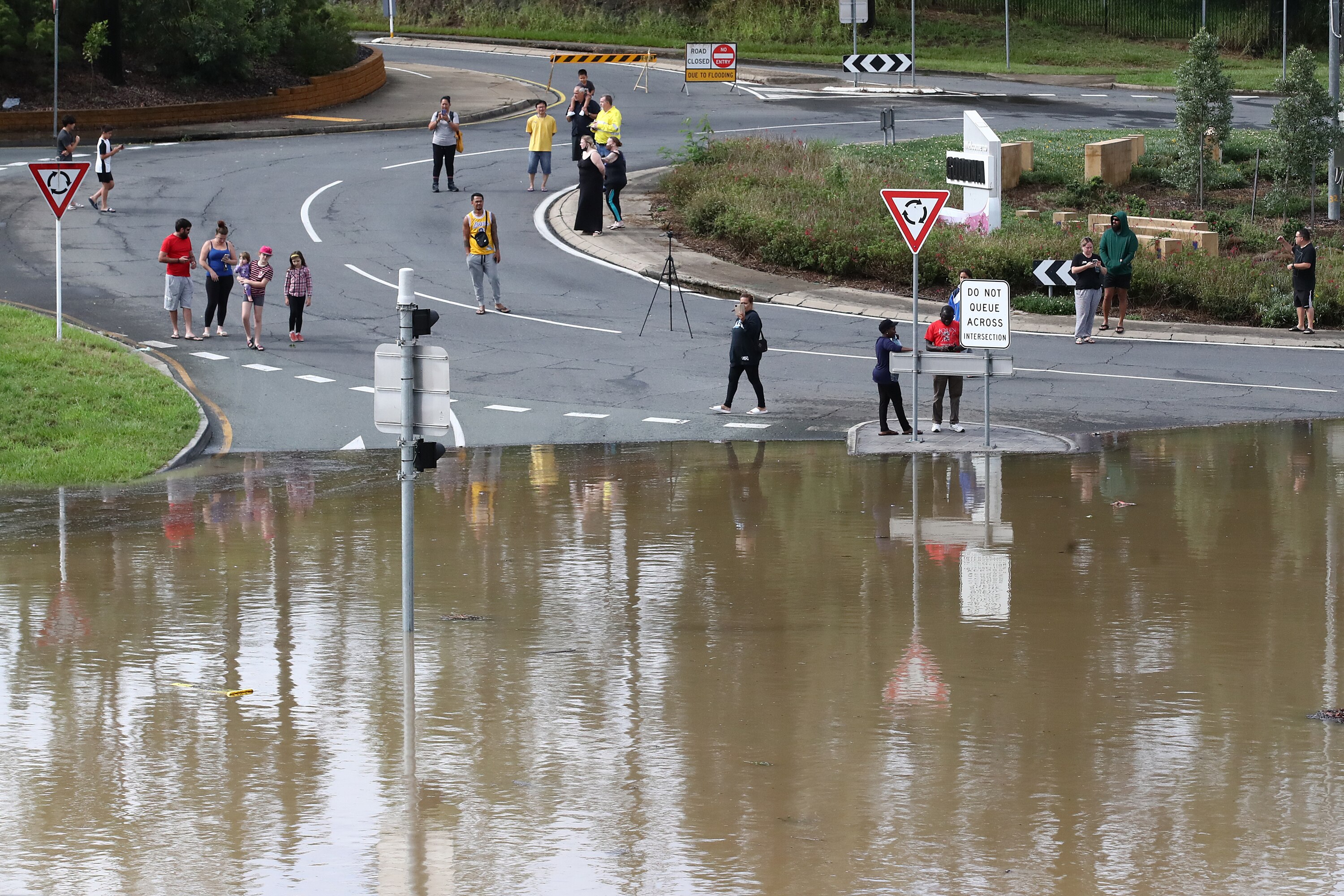 People stand and watch flood waters as a street is inundated.