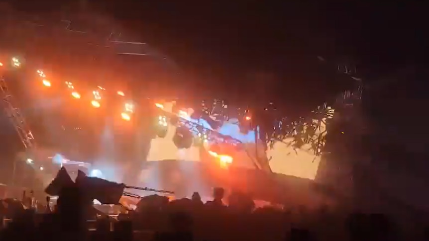 A slightly blurry screenshot shows a metal stage structure leaning at an awkward angle over a crowd, mid-collapse.