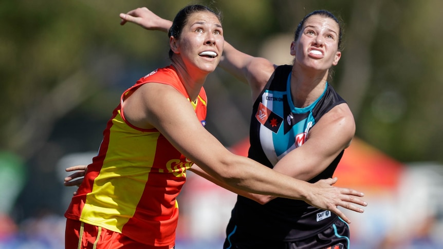 A Gold Coast Suns AFLW player and a Port Adelaide opponent push against each other ahead of a contest. 