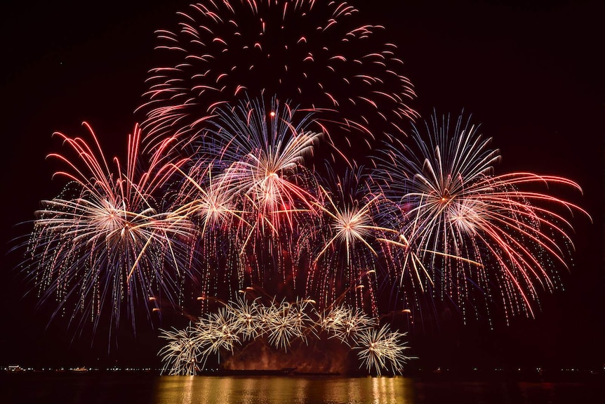 Blue, red and orange fireworks make an umbrella shape over a clear Manila Bay.