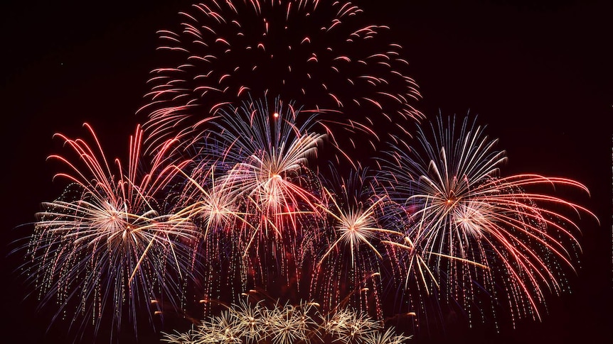 Blue, red and orange fireworks make an umbrella shape over a clear Manila Bay.