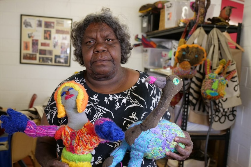 An Aboriginal woman stands with art she has made using a mix of materials including brightly coloured yarn