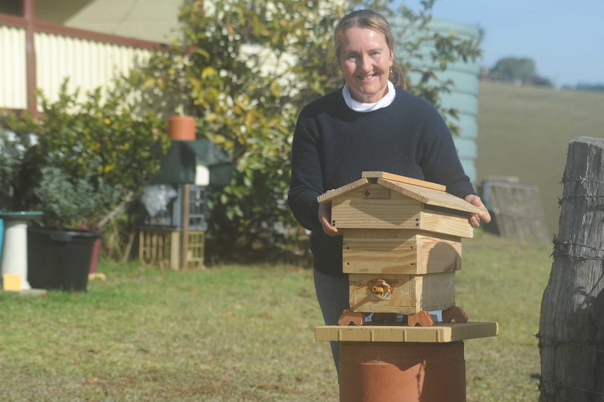 A smiling woman in a backyard with a native bee hive.