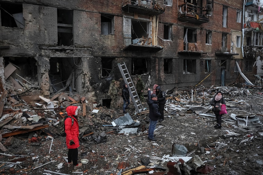 当地居民站在被炮击摧毁的公寓楼附近。