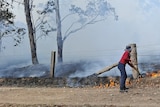 A woman shoveling dirt onto a burning fire near the fence line, smoke obscuring the horizon. 