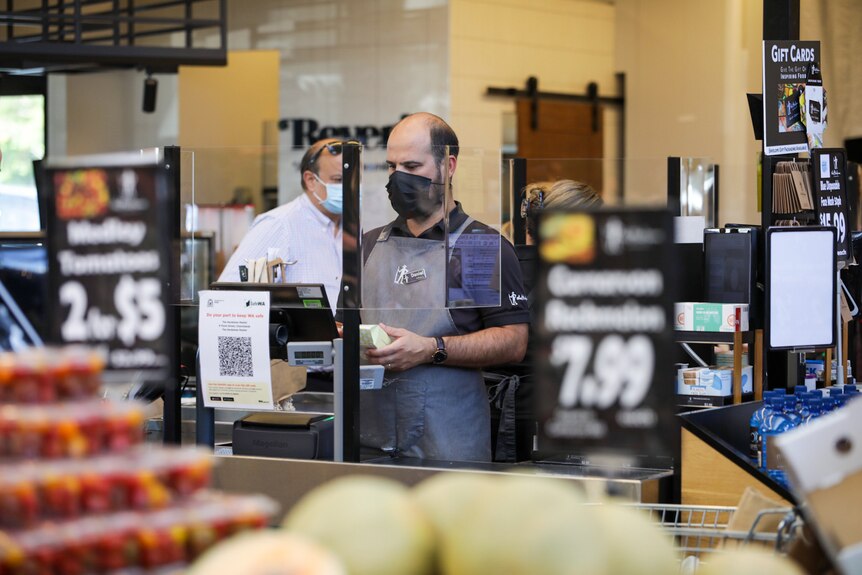 A man working at a supermarket checkout wearing a black mask.