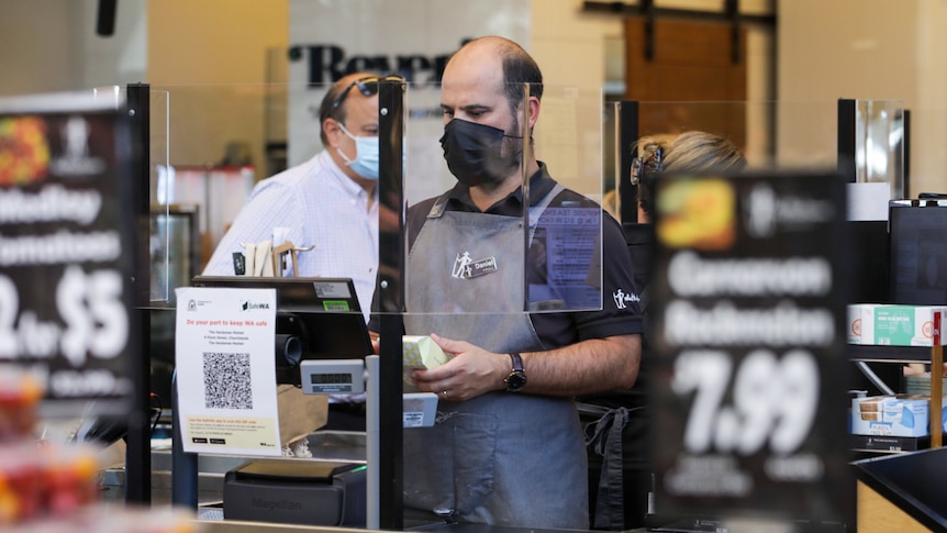 A man working at a supermarket checkout wearing a black mask.
