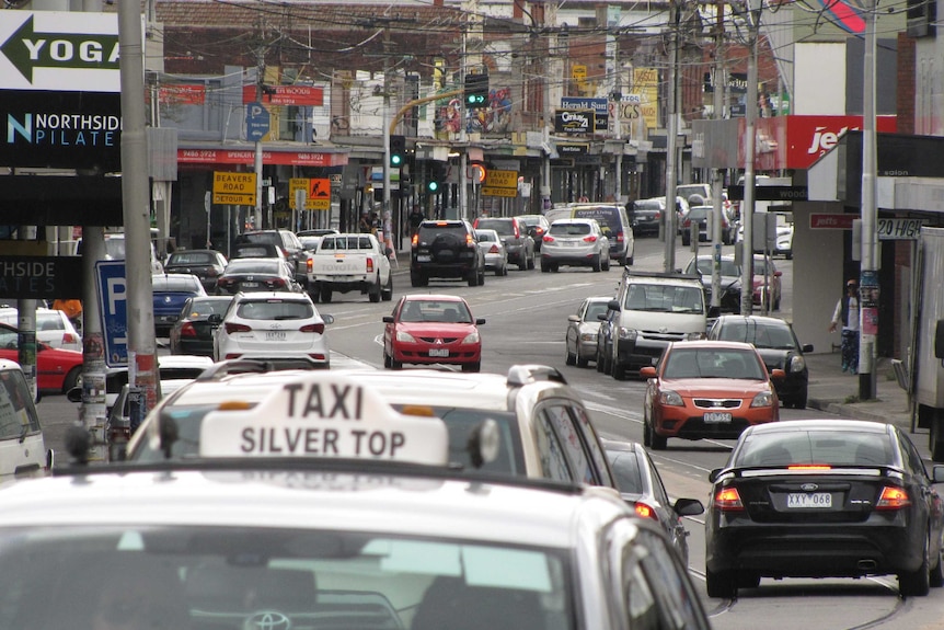 Traffic on busy High St in Northcote with a taxi in the foreground.