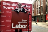 Jay Weatherill standing at a red South Australian Labor podium announcing a policy.
