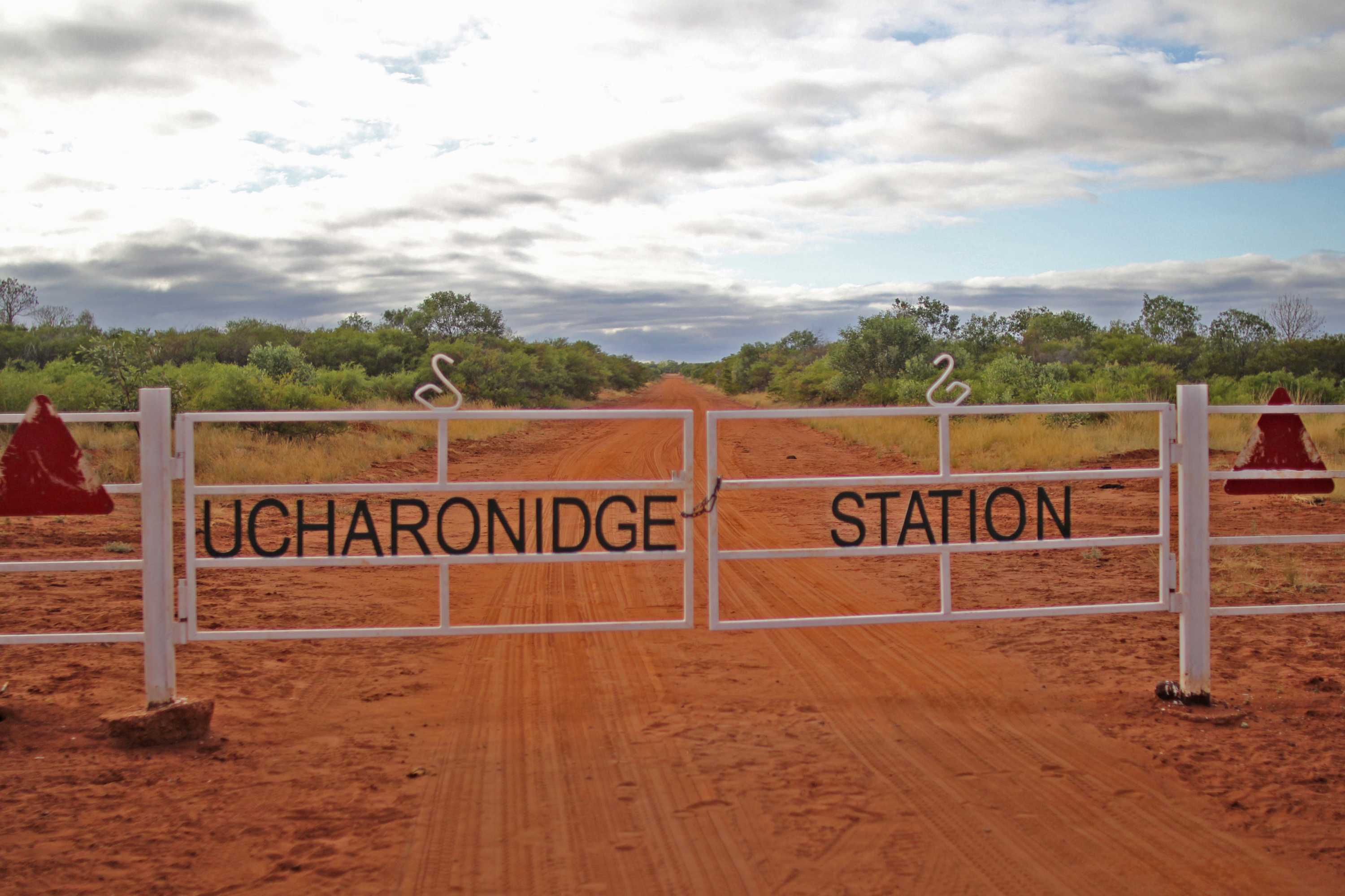 a white gate, reading Ucharonidge Station with a road and bushes in the background.