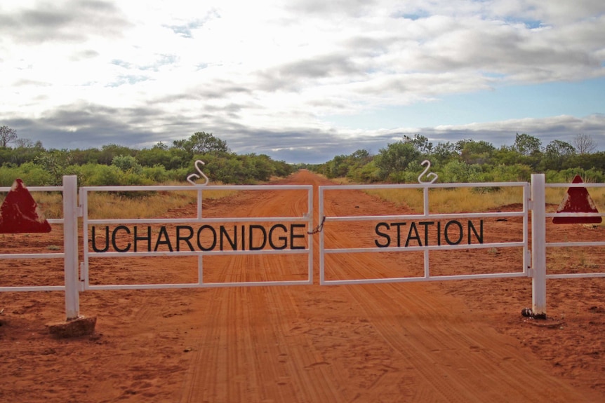 a white gate, reading Ucharonidge Station with a road and bushes in the background.