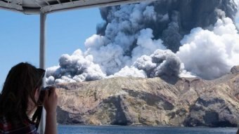 A woman on a boat takes a photo of the volcano on White Island just moments after it erupted.