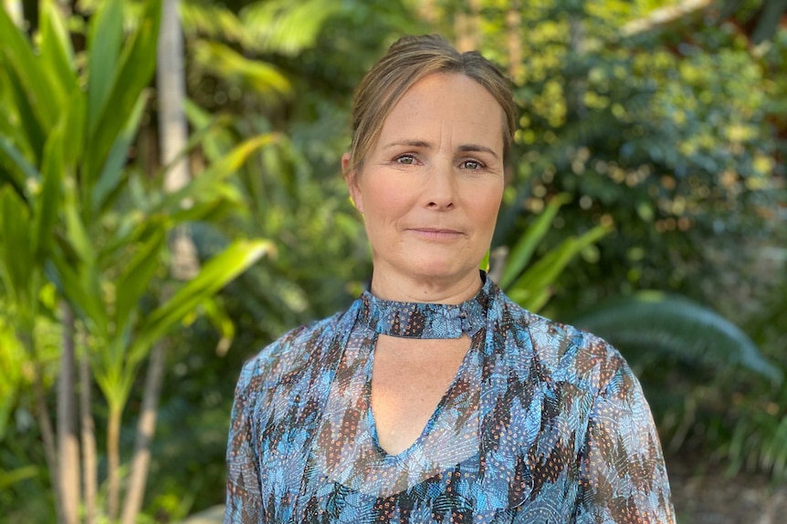 Jacqui Barker wears a blue shirt and stands in a garden.