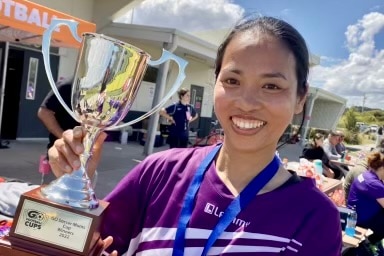 A Vietnamese woman in purple shirt holding a trophy. 