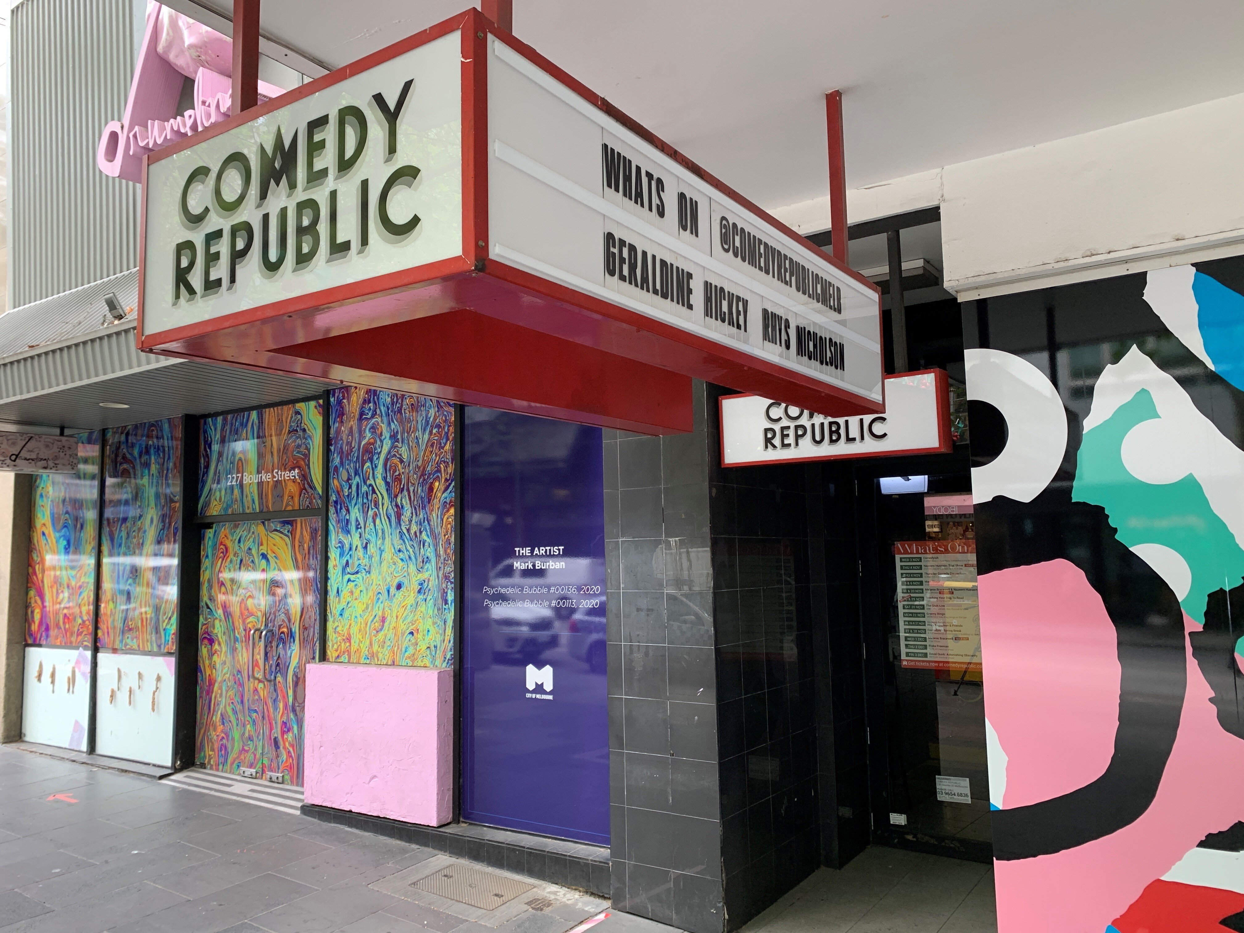 A big electronic sign saying Comedy Republic hangs from the ceiling in front of a colourful wall.