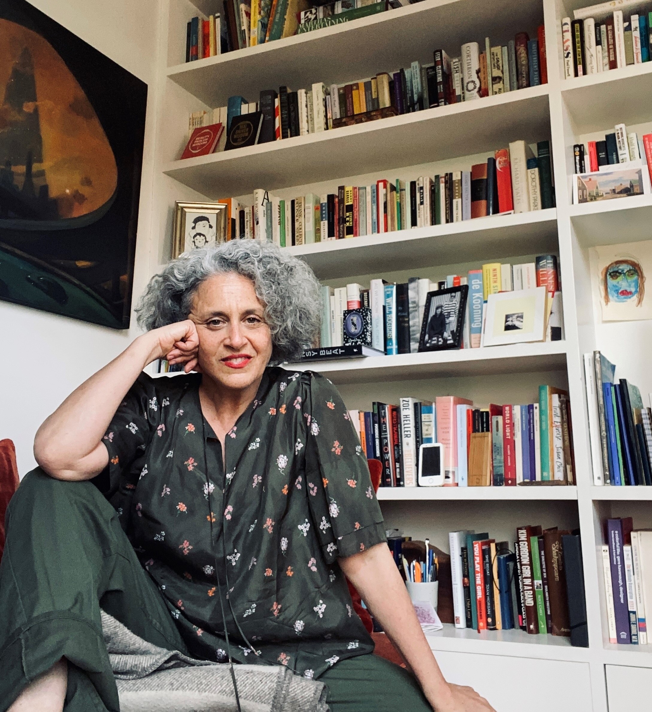 A middle-aged woman sits in front of a bookcase.