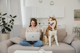 A woman sitting on a couch with a husky