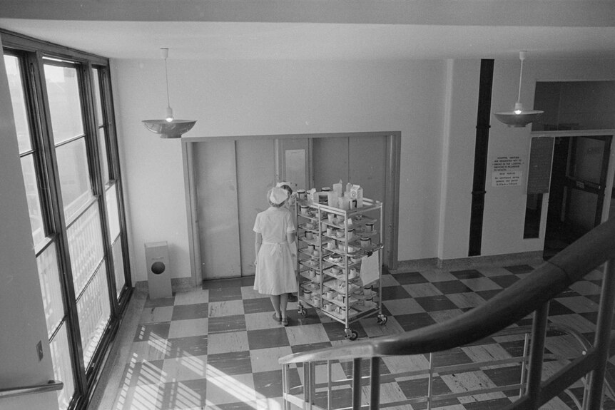 Nurses wheel a trolley filled with crockery into a lift at a hospital.