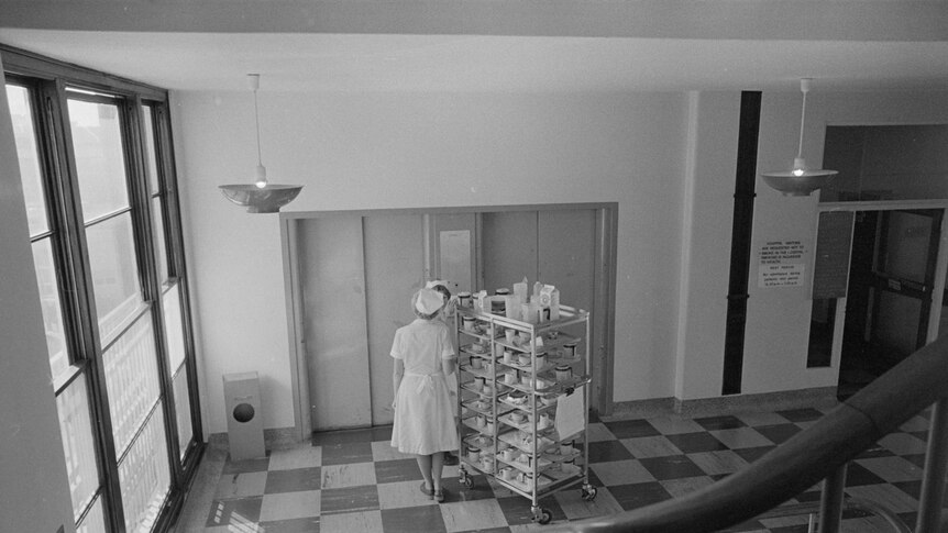 Nurses wheel a trolley filled with crockery into a lift at a hospital.