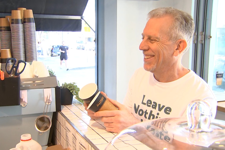 A man smiling holding coffee cups at a cafe counter